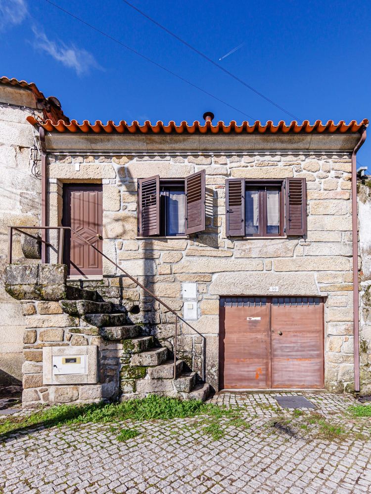 Fachada em granito da moradia em Benagouro, com escada de pedra, portadas de madeira e portão da garagem